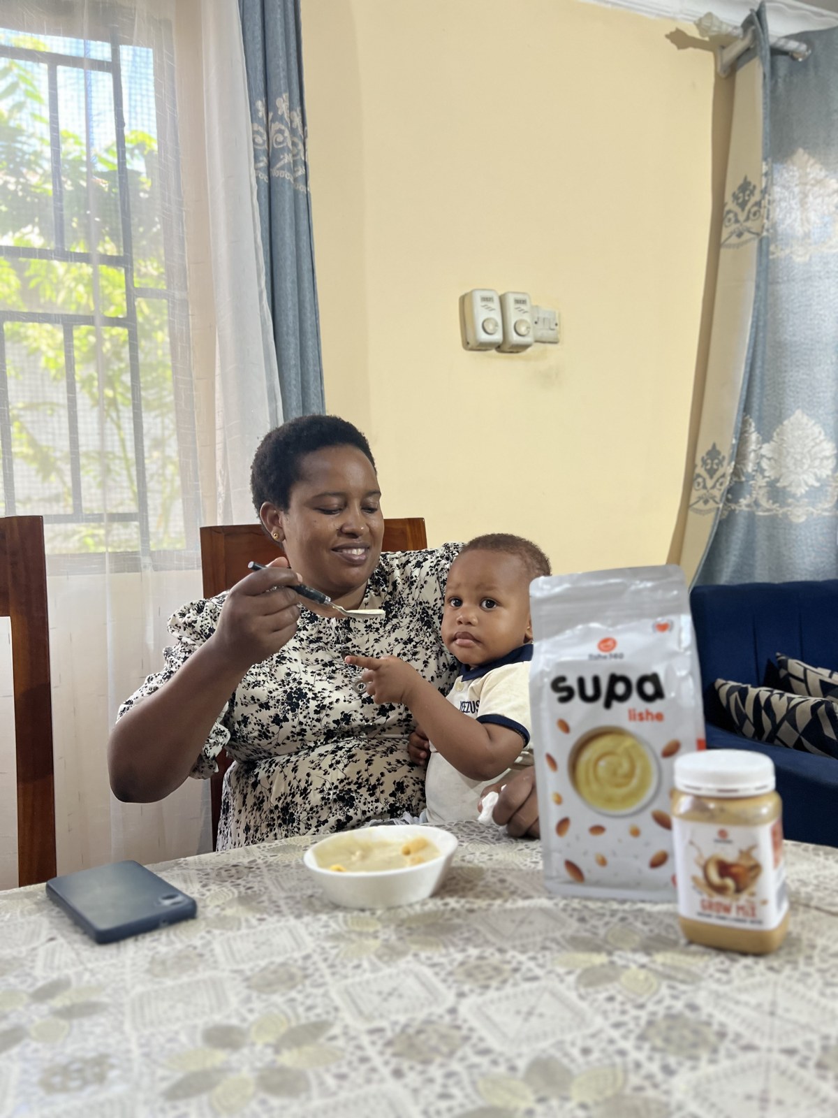 A caregiver feeding her child, with Lishe360 products on the table
